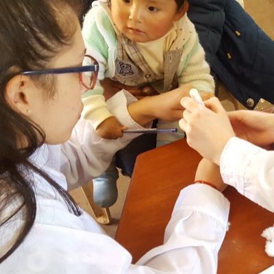Midwifery interns test an infant's iron levels during an outreach in Peru. Two students doing Midwifery internships in Peru test an infant's iron levels at a clinic.
